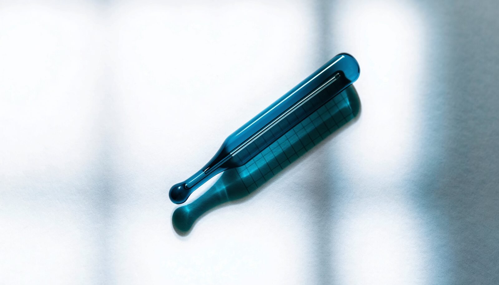 A glass clinical thermometer lying at an angle on gridded temperature-chart paper in soft daylight